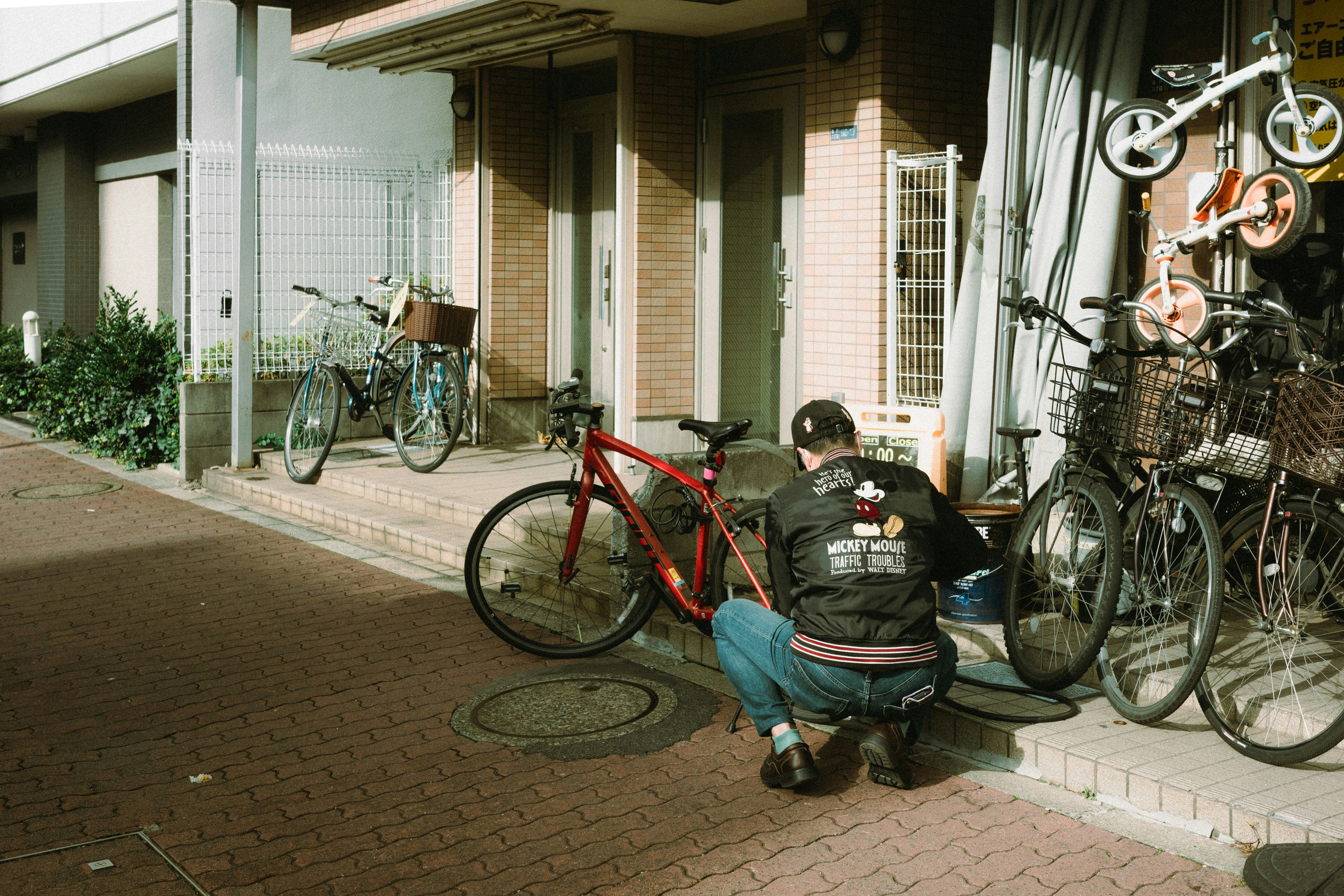 A man crouching by bicycles outside a Japanese shop